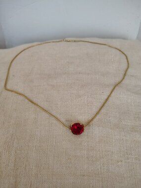 Gold tone pendant necklace featuring a faceted prong mounted red glass stone